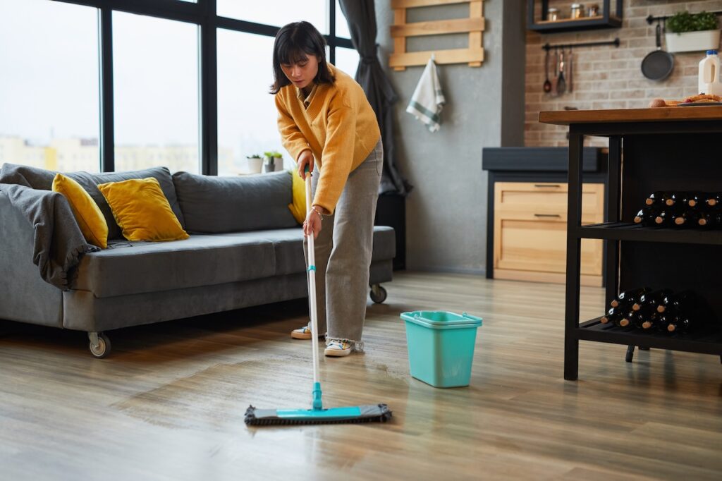 woman at home performing hardwood flooring maintenance by cleaning kitchen area