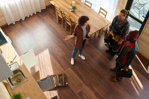 Overhead angle of a woman hiring professionals for hardwood floor repair