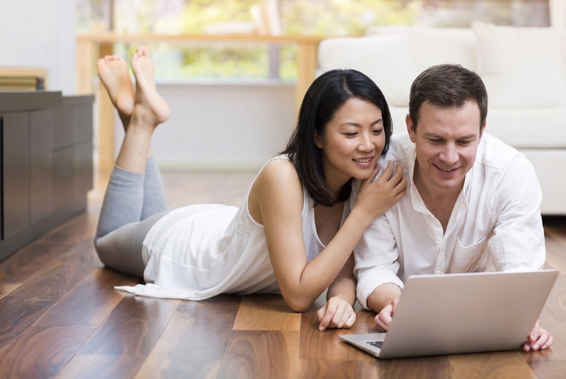 Couple relaxing with a laptop on a dark walnut hardwood floor at home