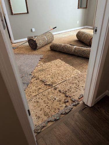 Old carpet and padding rolled up and removed from a Duluth, GA bedroom, subfloor exposed before new carpet installation
