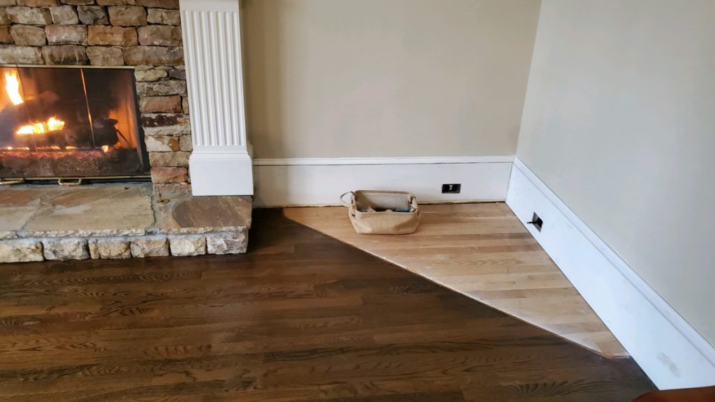 Oak hardwood floor being refinished beside a lit stone fireplace and its raised stone hearth