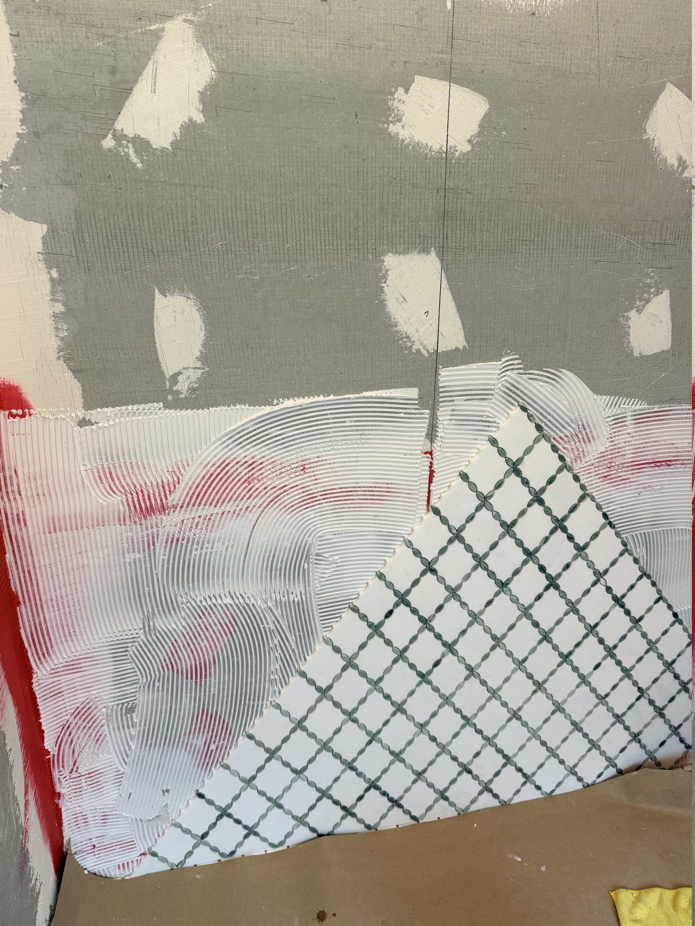 Red waterproofing membrane and combed thinset behind trellis-pattern tile going up in a Roswell, GA bathroom remodel by Atlanta Floor One